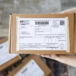 Tangan memegang paket kiriman dengan label pengiriman, siap untuk dikembalikan